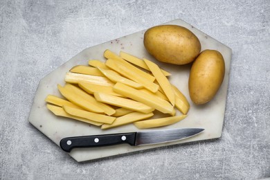 Photo of Whole and cut raw potatoes with knife on light grey table, top view. Cooking delicious French fries