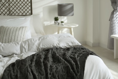 Photo of Comfortable bed with warm knitted plaid in stylish room interior