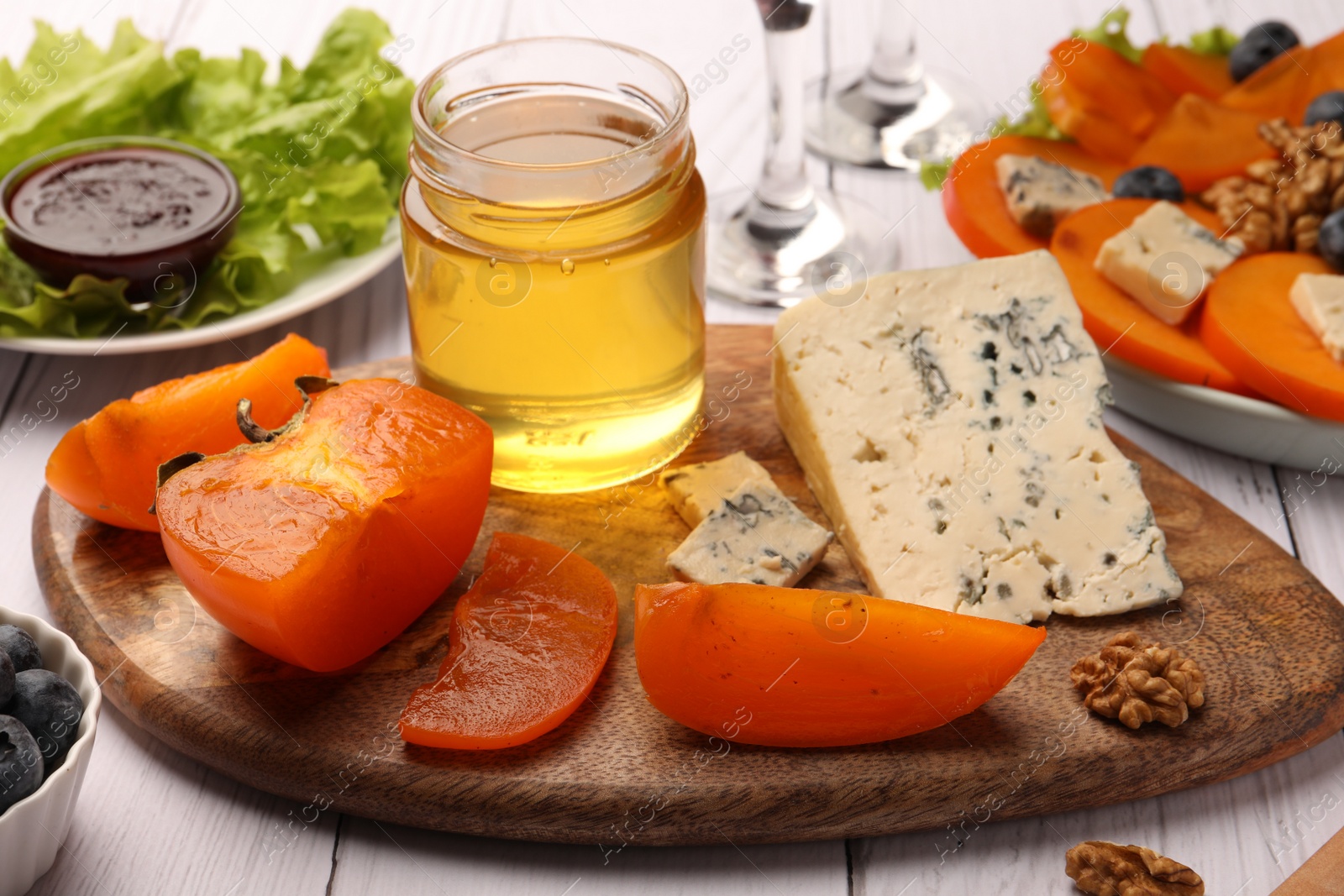 Photo of Delicious persimmon, blue cheese, honey and walnuts on white wooden table, closeup