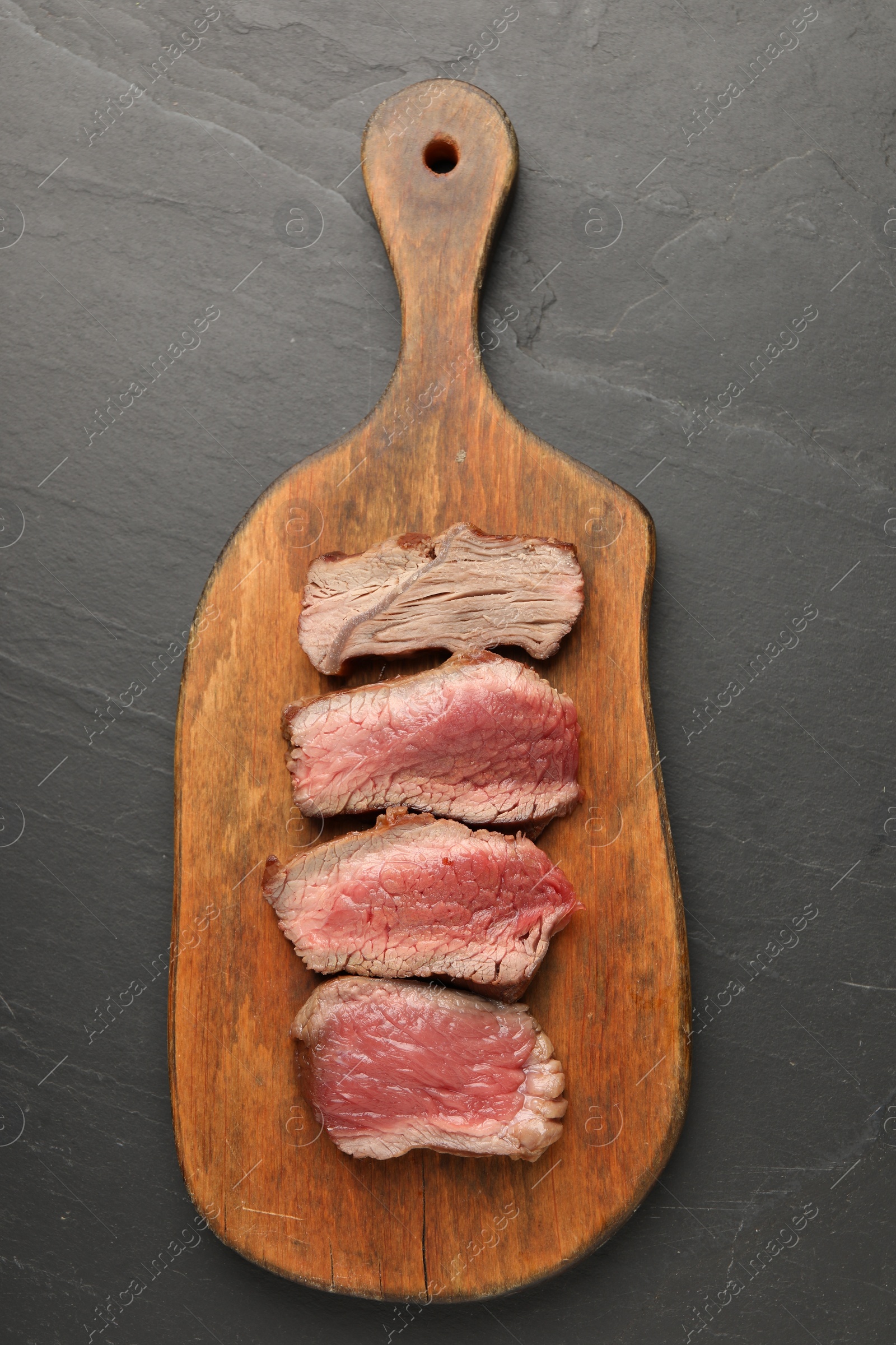 Photo of Delicious sliced beef tenderloin with different degrees of doneness on black table, top view