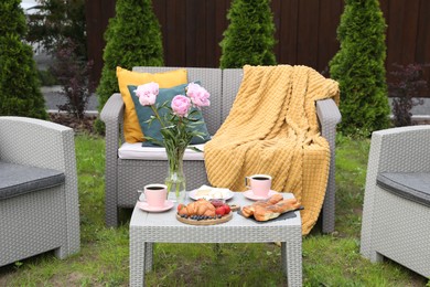 Photo of Breakfast served outdoors. Morning drink, food and vase with flowers on rattan table