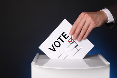 Man putting paper with word Vote and tick into ballot box on dark blue background