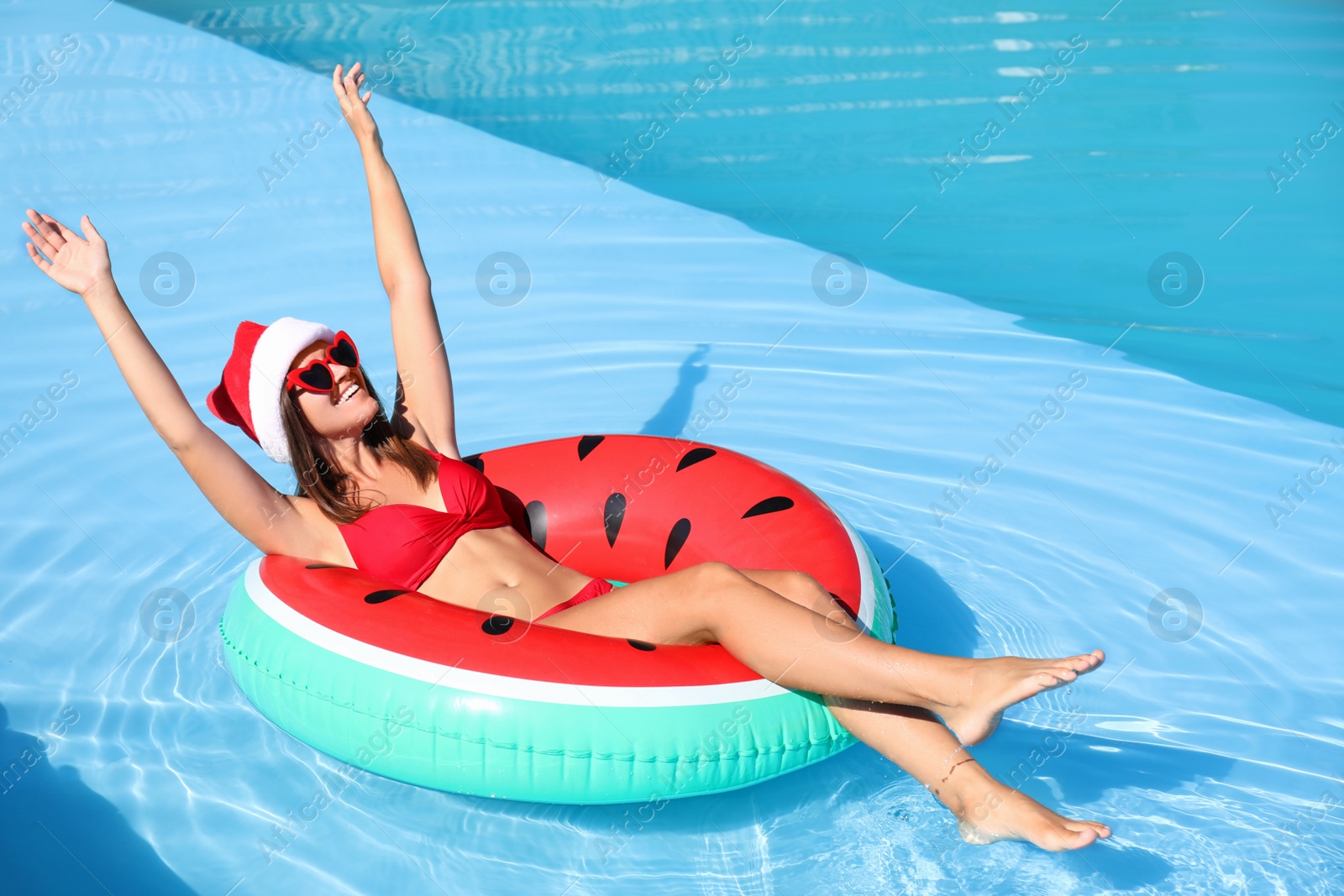 Photo of Young woman wearing Santa Claus hat on inflatable ring in swimming pool. Christmas vacation