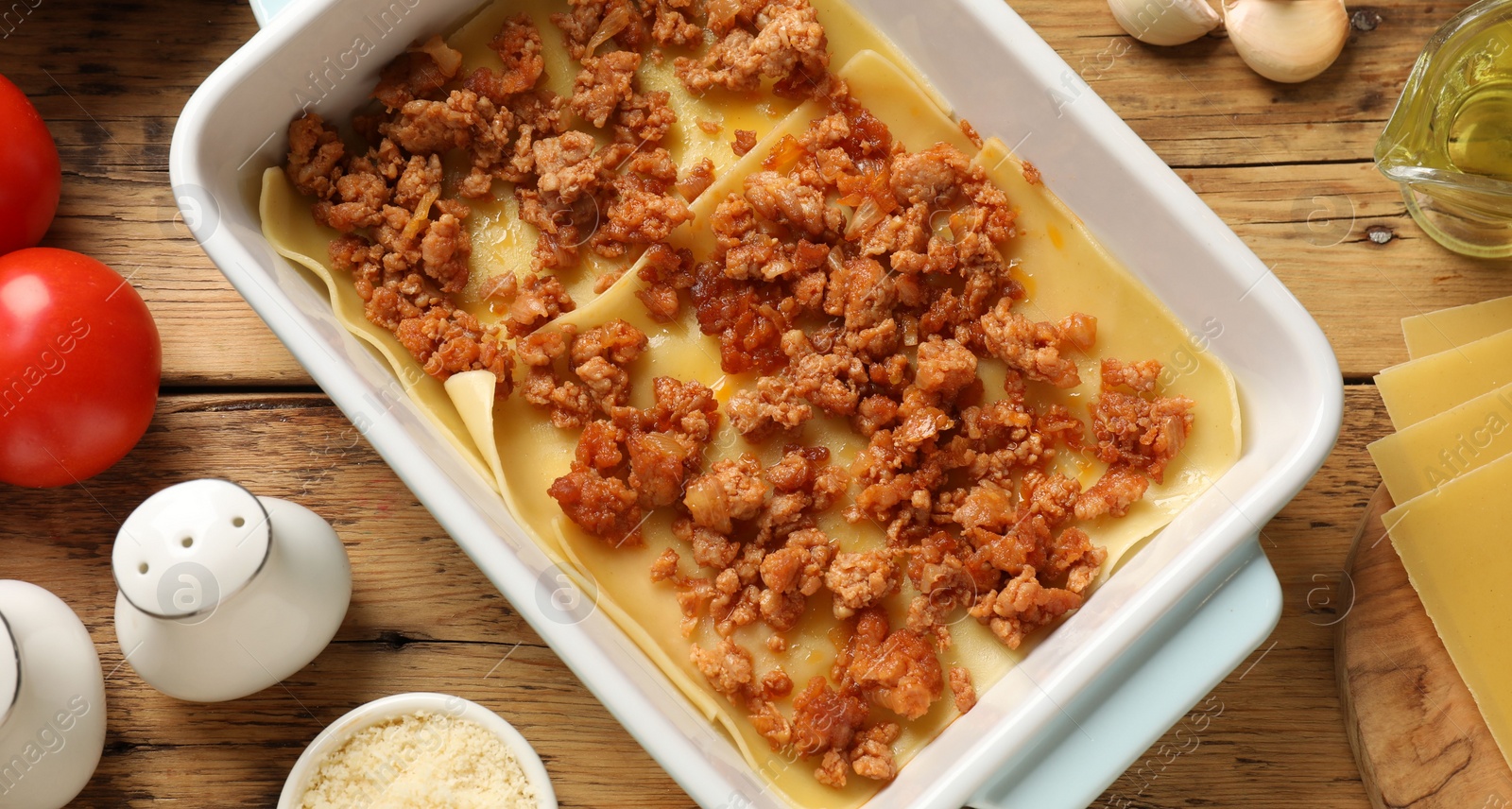 Photo of Cooking lasagna. Pasta sheets and minced meat in baking tray on wooden table, flat lay