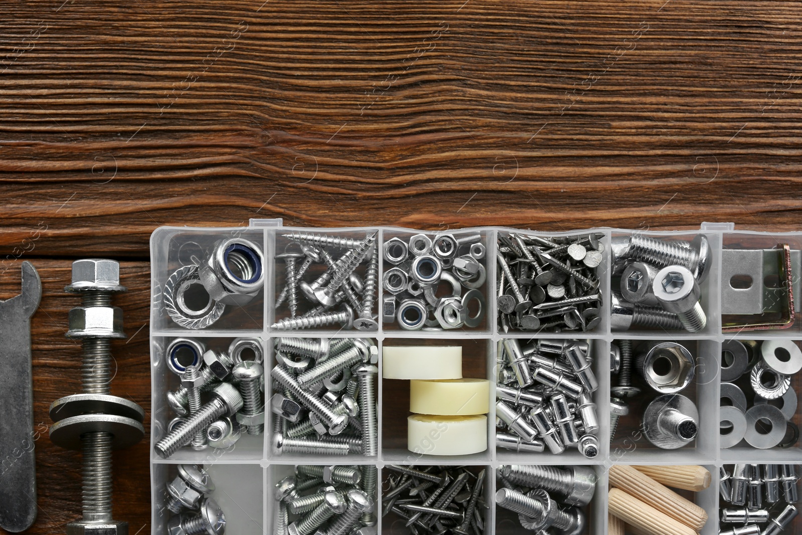 Photo of Plastic box with different furniture fittings and tools on wooden table, flat lay