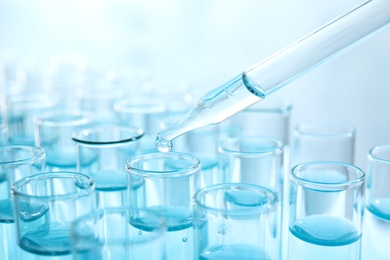 Dropping sample into test tube with light blue liquid, closeup