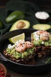 Delicious sandwiches with guacamole, shrimps and black sesame seeds in serving pan, closeup
