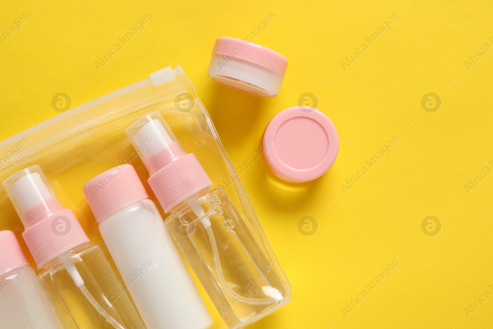 Photo of Plastic bag with cosmetic travel kit on yellow background, flat lay. Space for text