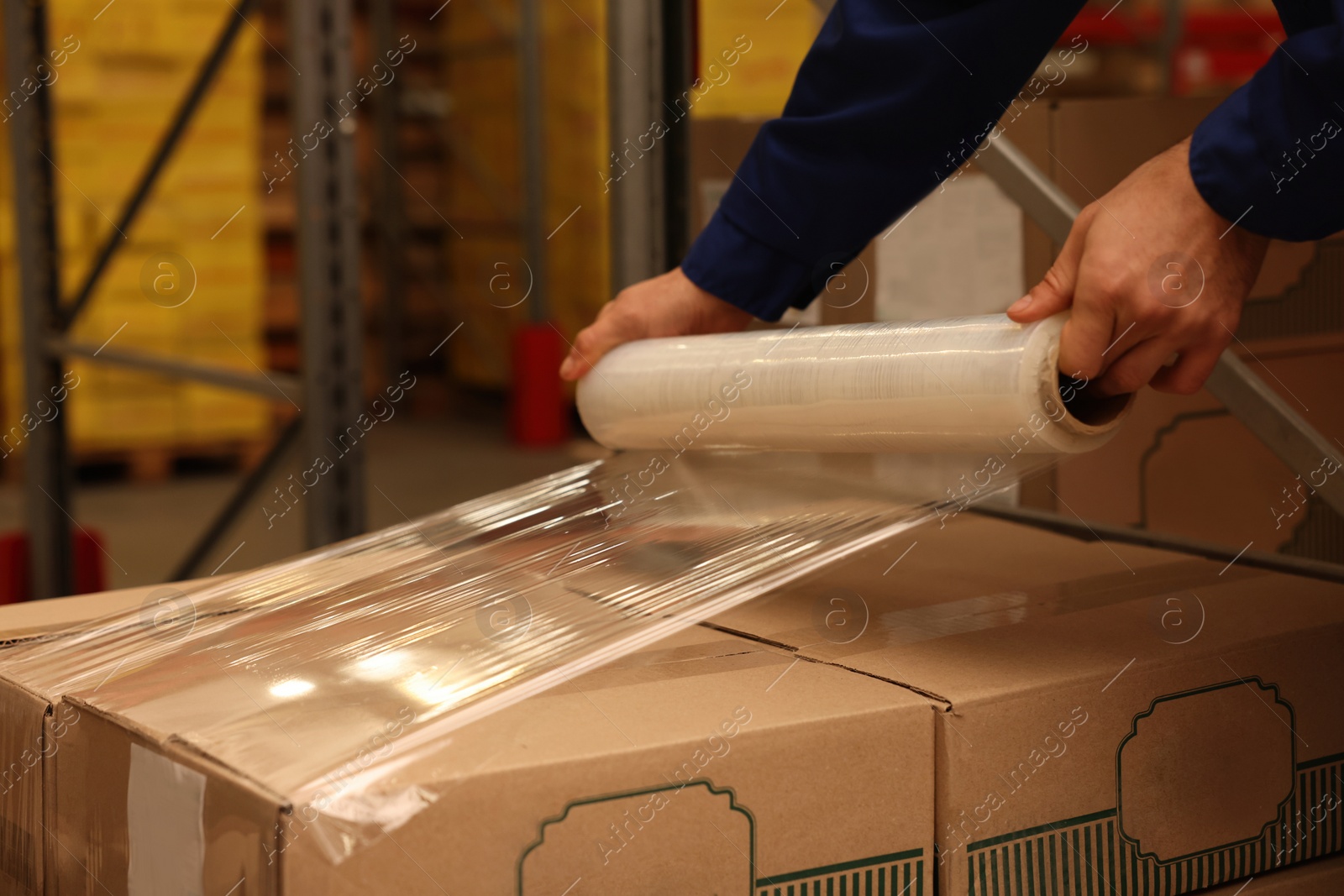 Photo of Worker wrapping boxes in stretch film at warehouse, closeup