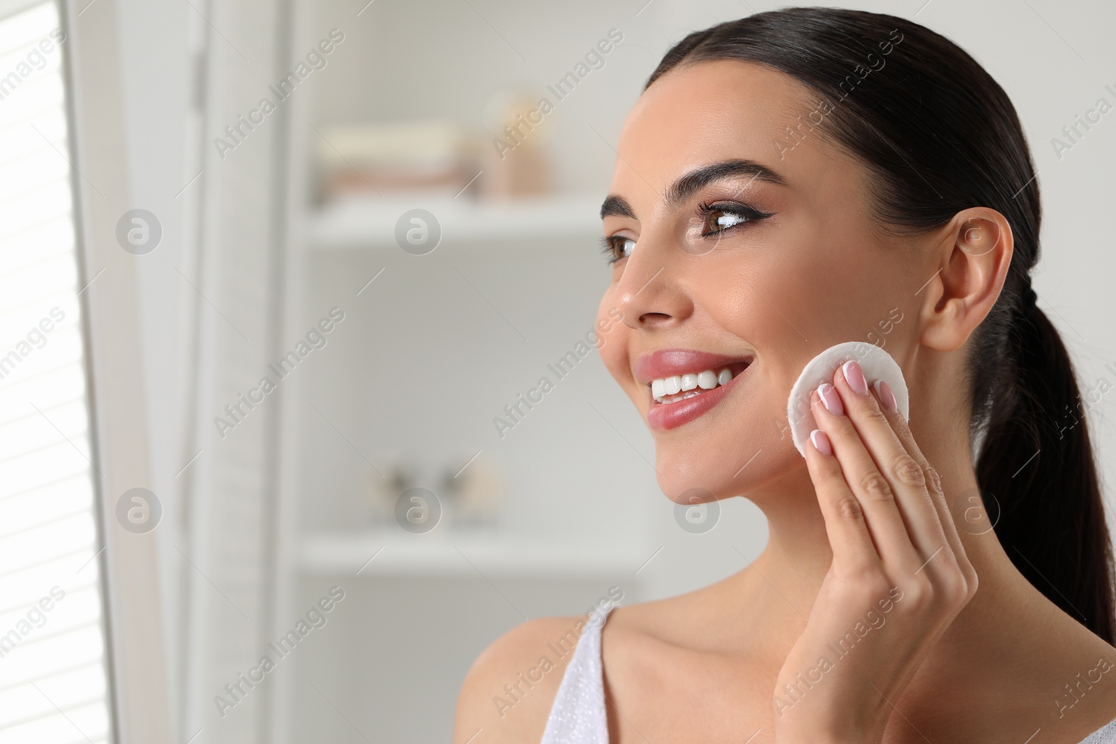 Photo of Beautiful woman removing makeup with cotton pad indoors, space for text