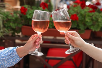 Photo of Women clinking glasses with rose wine in outdoor cafe, closeup