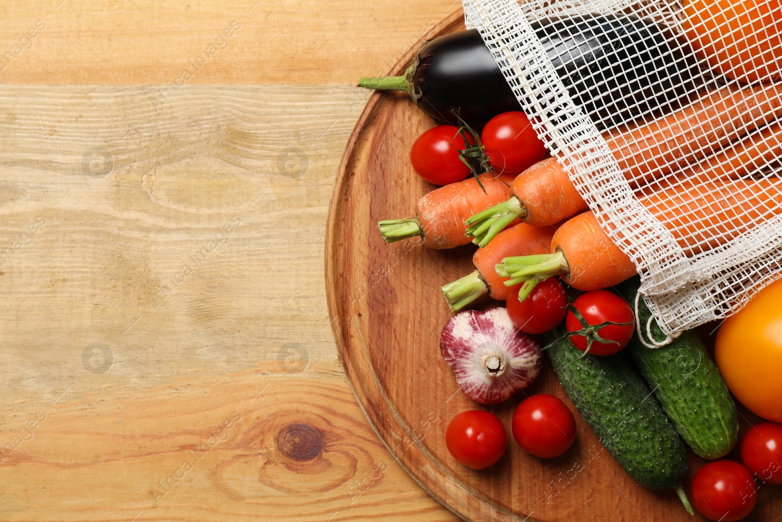 Photo of Many different vegetables and net bag on wooden table, top view. Space for text