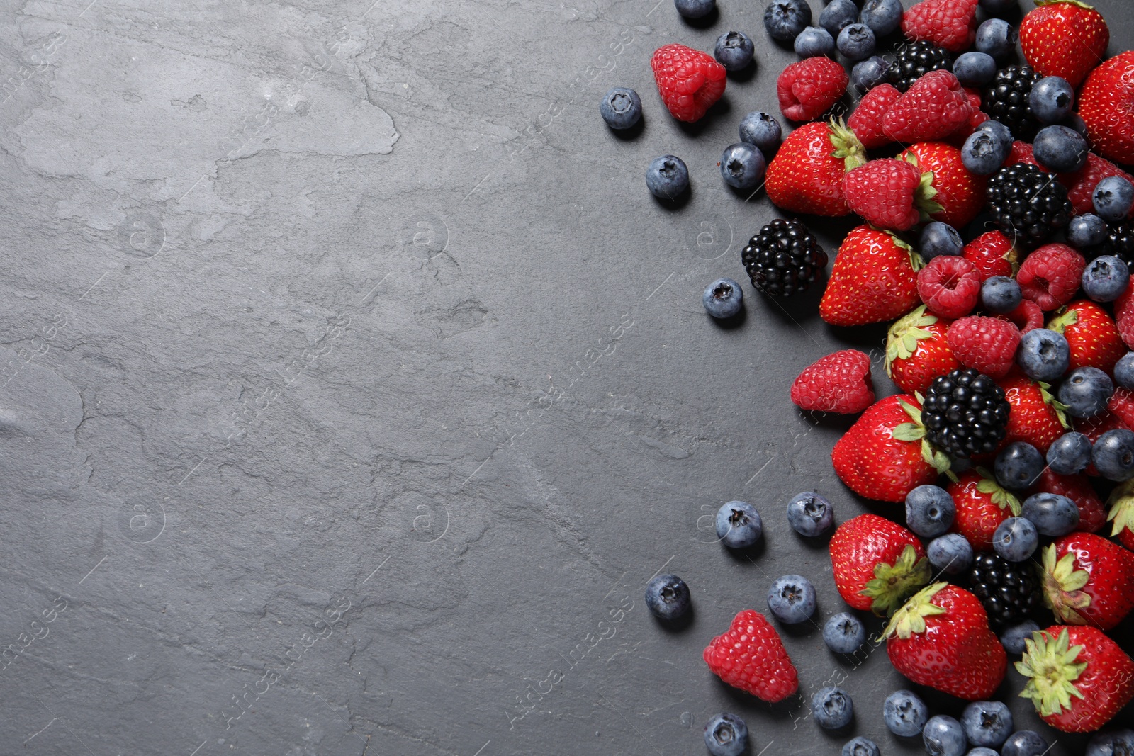 Photo of Many different fresh ripe berries on dark grey table, flat lay. Space for text