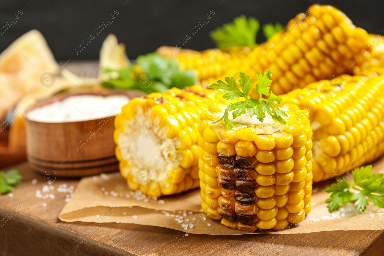 Photo of Delicious grilled corn cobs on wooden table, closeup