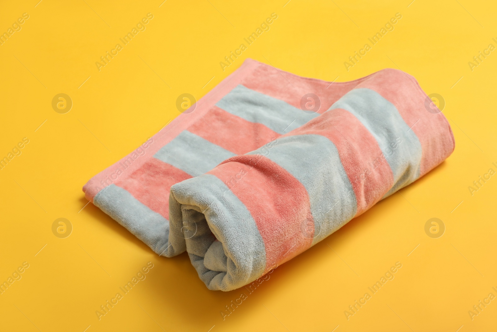 Photo of Rolled striped beach towel on yellow background