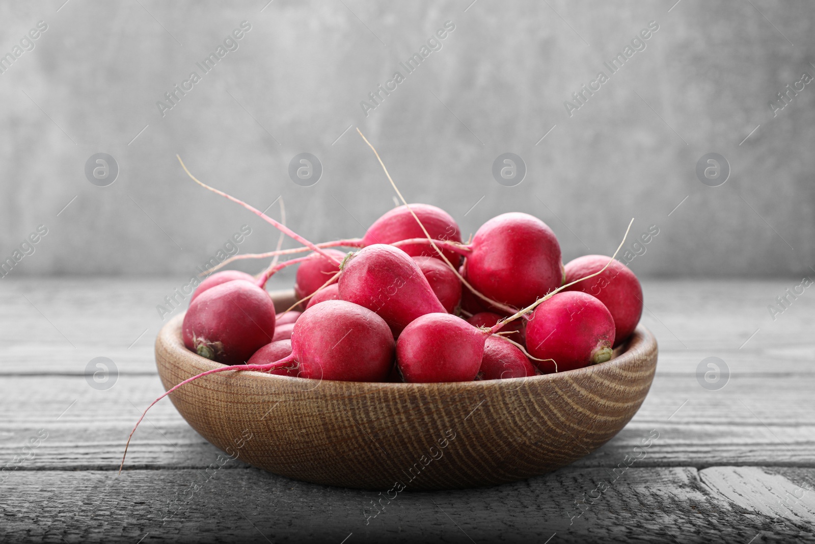 Photo of Bowl with fresh ripe radishes on grey wooden table