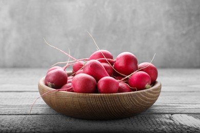 Bowl with fresh ripe radishes on grey wooden table