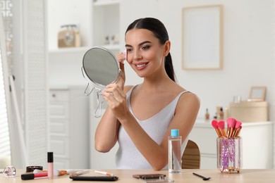 Beautiful woman removing makeup with cotton pad at table in room