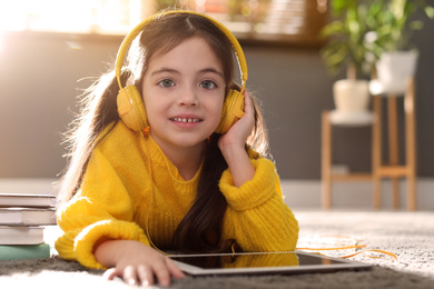 Cute little girl with headphones and tablet listening to audiobook at home