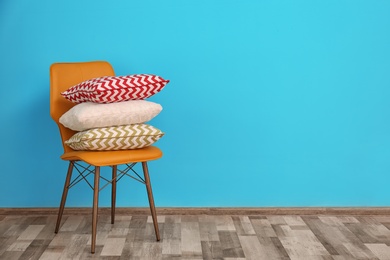 Photo of Chair with different pillows near color wall in room