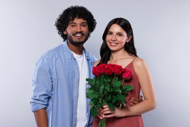 International dating. Happy couple with bouquet of roses on light grey background