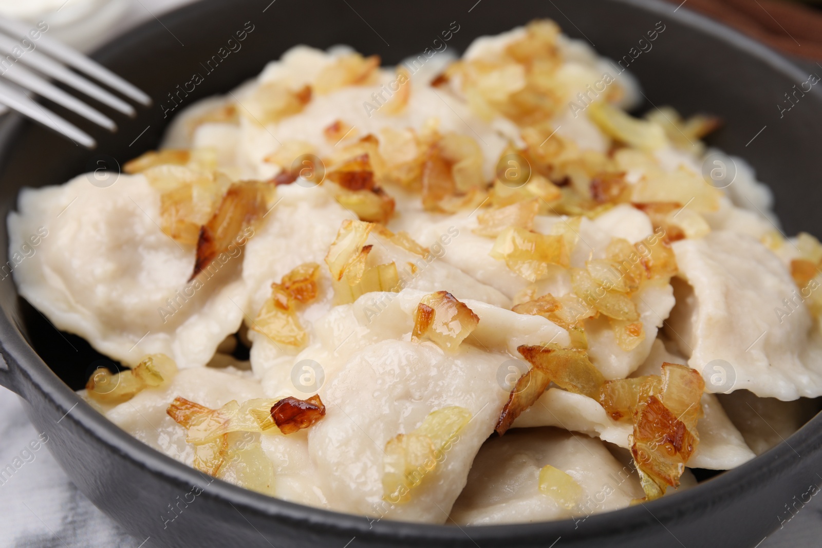 Photo of Cooked dumplings (varenyky) with tasty filling and fried onions in frying pan, closeup