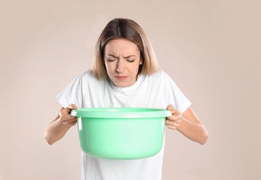 Woman with basin suffering from nausea on beige background. Food poisoning