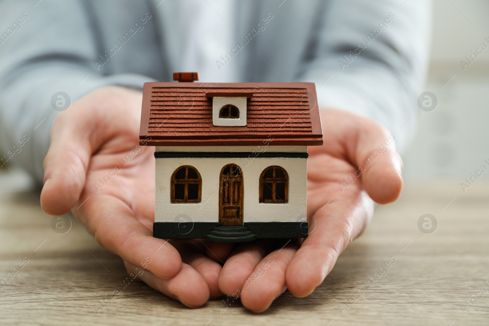 Photo of Real estate agent holding house model at wooden table, closeup