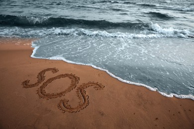 Image of SOS message drawn on sandy beach near sea