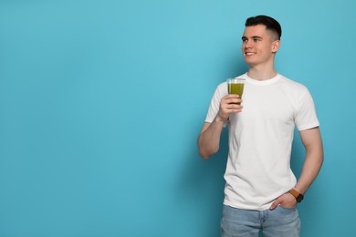 Photo of Handsome young man with glass of juice on light blue background, space for text