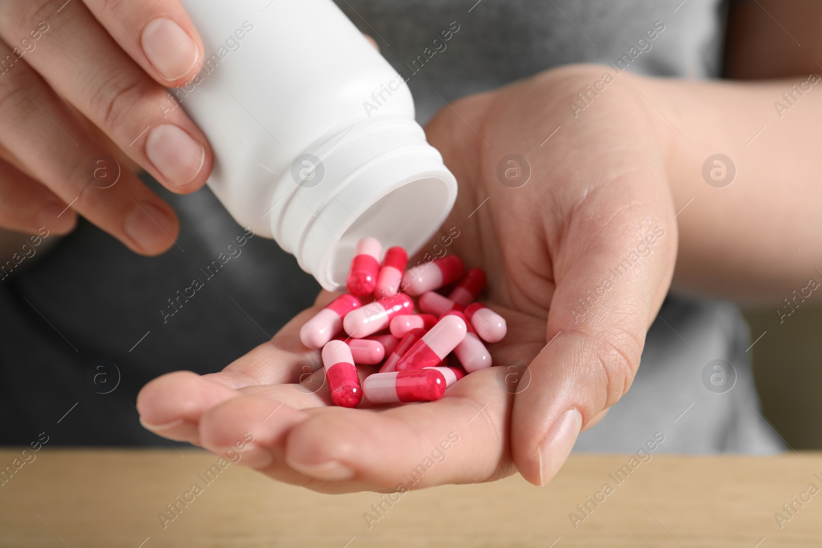 Photo of Woman pouring pills from bottle at table, closeup
