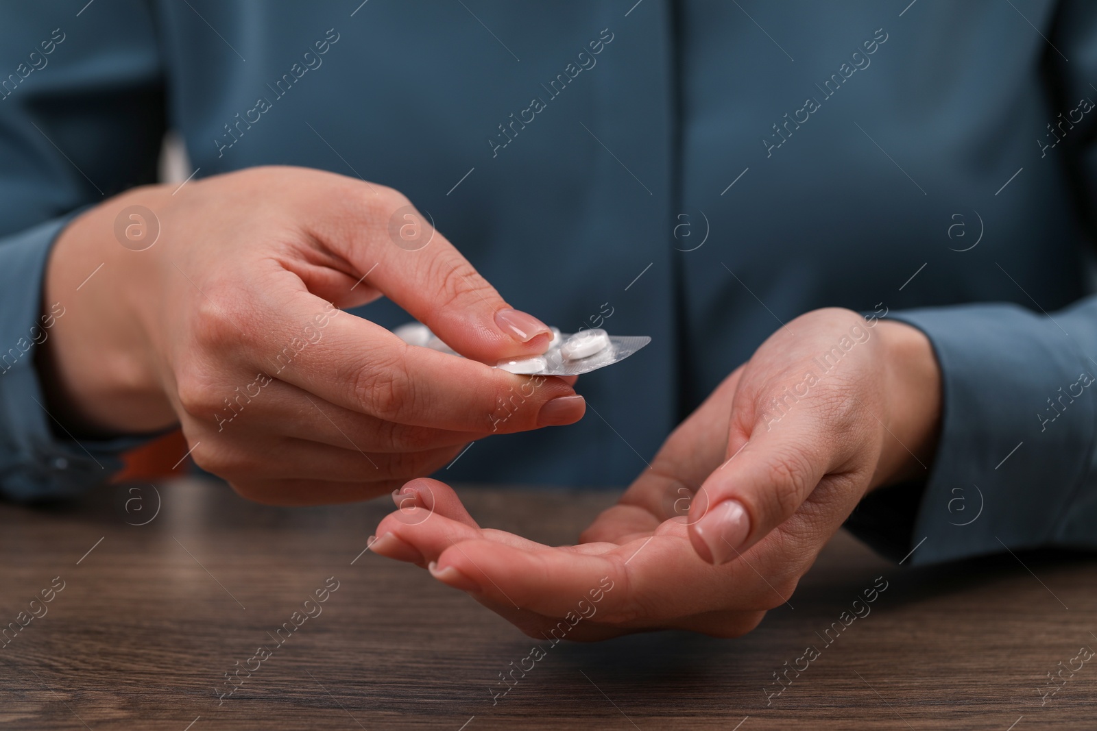 Photo of Woman taking antidepressant pill out from blister at wooden table, closeup