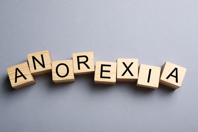 Word Anorexia made of wooden cubes with letters on light grey background, flat lay