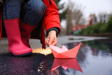 Photo of Little girl playing with paper boat near puddle outdoors, closeup