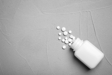 Container with pills on grey background, flat lay