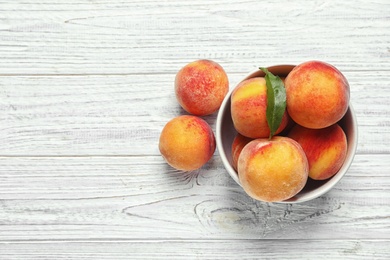 Bowl with delicious ripe peaches on wooden background, top view