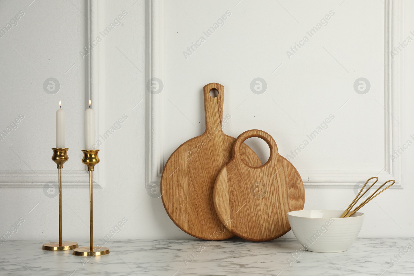 Photo of Wooden cutting boards, bowl and candlesticks on white marble table
