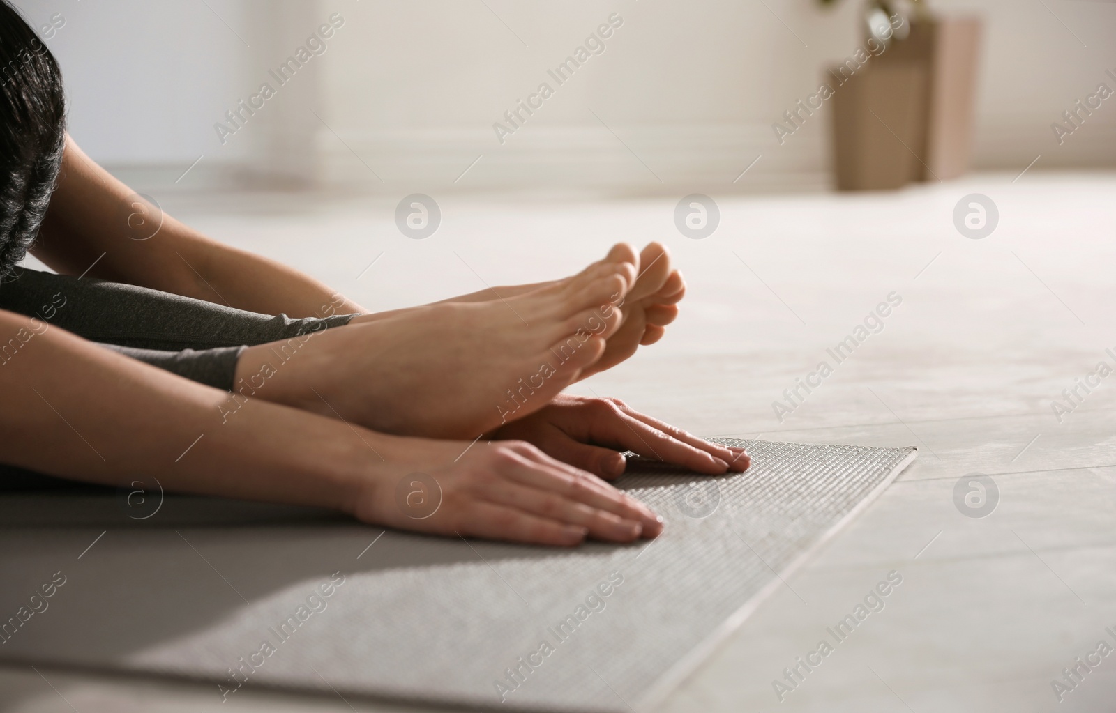 Photo of Young woman practicing seated forward bend asana in yoga studio, closeup. Paschimottanasana pose