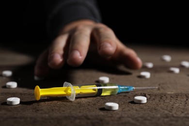 Photo of Addicted man reaching to drugs at wooden table, focus on syringe