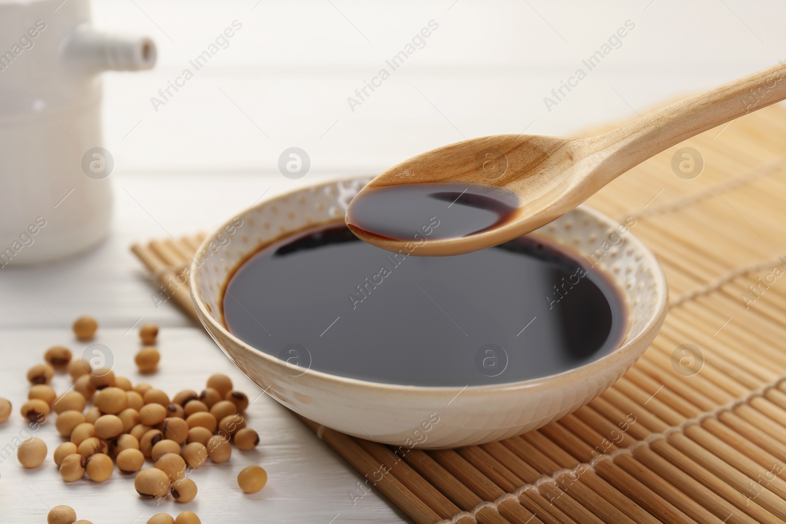 Photo of Taking tasty soy sauce from bowl with spoon on white wooden table, closeup
