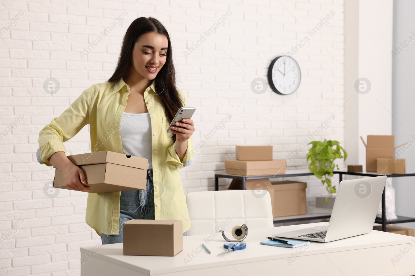 Photo of Seller with laptop and parcels using smartphone in office. Online store