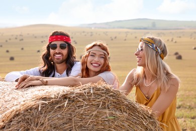Happy hippie friends near hay bale in field