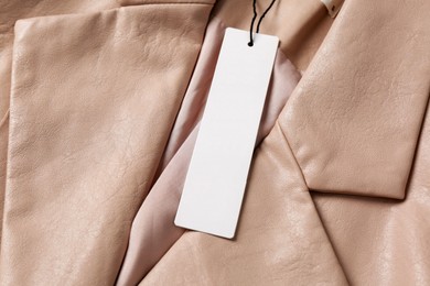 Photo of Blank white tag on beige leather jacket, top view. Space for text