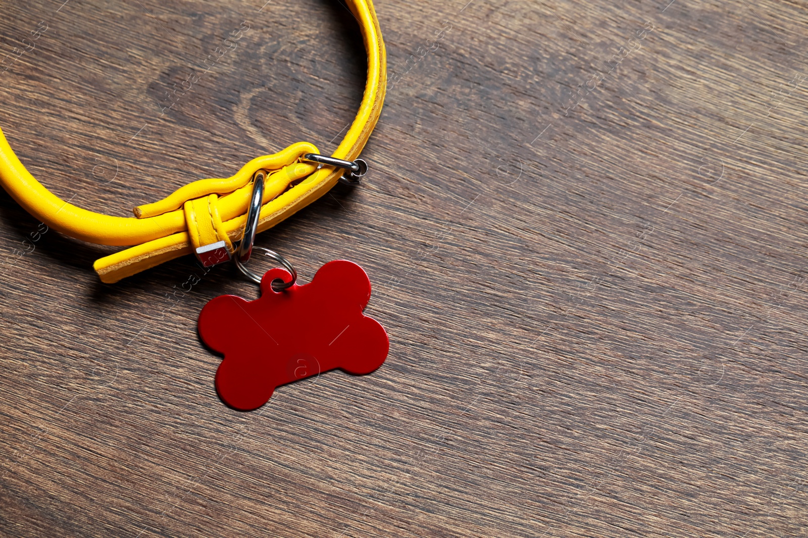 Photo of Yellow leather dog collar with red tag in shape of bone on wooden table, top view. Space for text