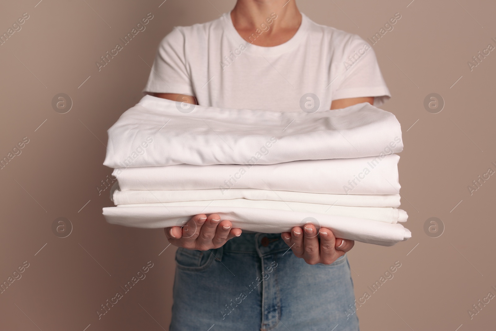 Photo of Woman holding stack of clean bed linens on beige background