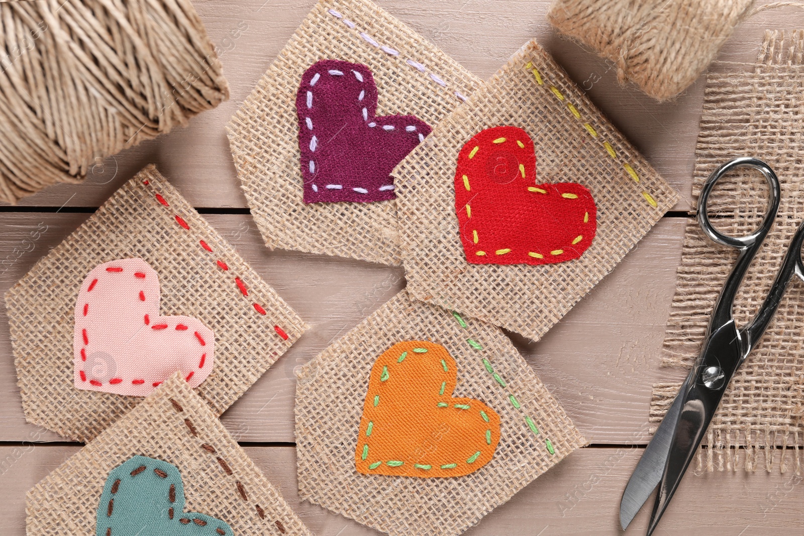 Photo of Pieces of burlap fabric with hearts and scissors on wooden table, flat lay