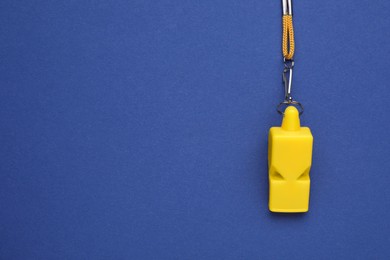 Photo of One yellow whistle with cord on blue background, top view. Space for text