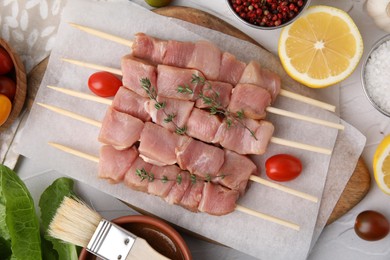 Photo of Flat lay composition of skewers with cut raw meat, thyme, tomatoes and marinade on light table