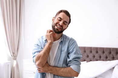 Photo of Young man scratching neck indoors. Allergies symptoms