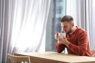 Young man with cup of hot drink near window at cafe